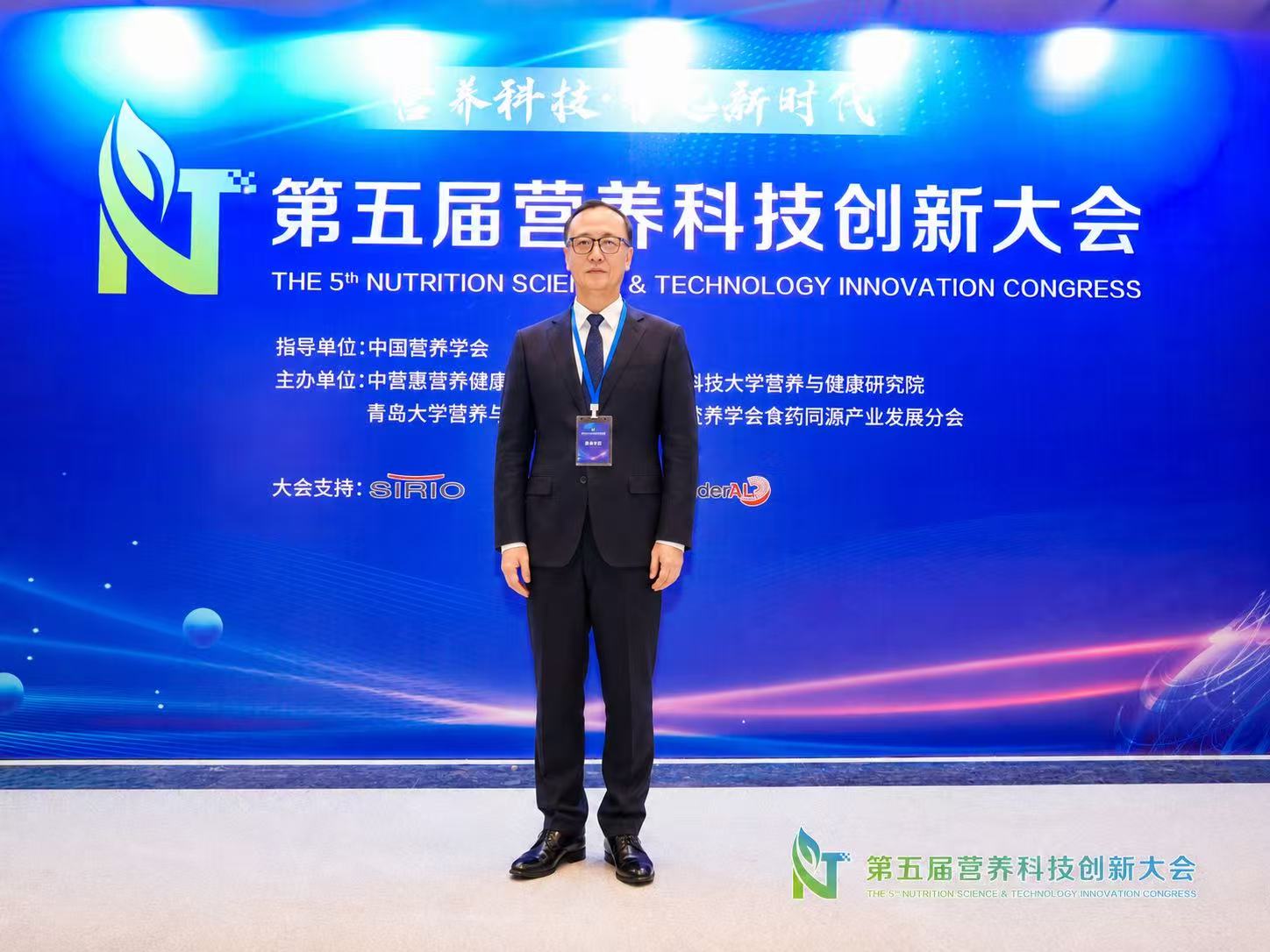 刘老师站在营养科技大会会场背景前的近照